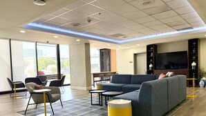 A modern lounge area with seating, a flat-screen TV, and a large window. - City Express by Marriott I-10 West Energy Corridor (Houston)