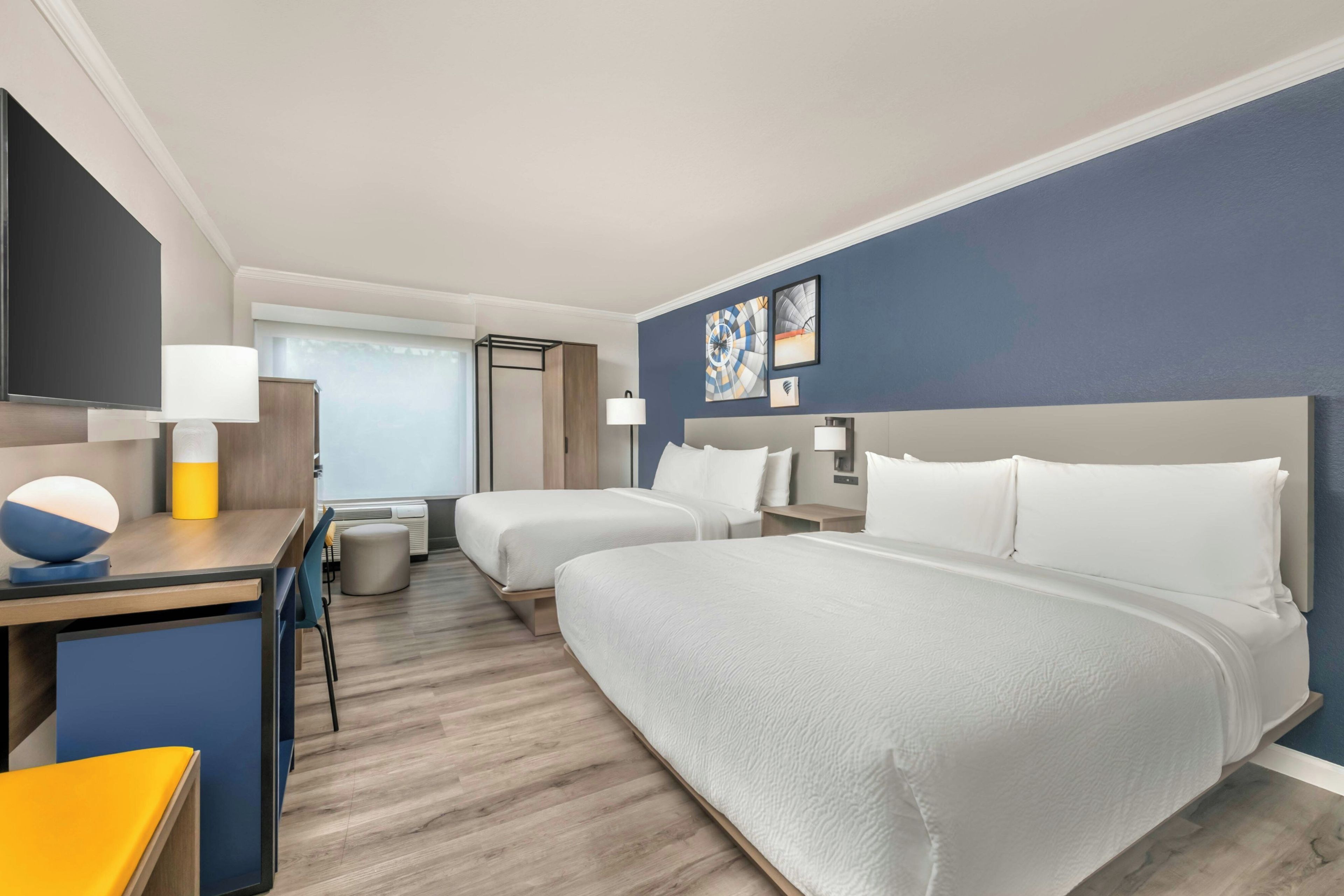 Een hotelkamer met twee bedden, een bureau, een stoel, een televisie en kunst aan de muur.