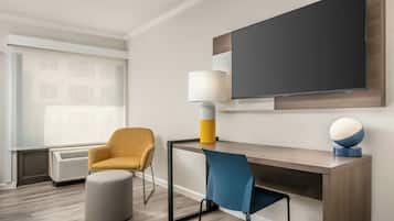 A modern hotel room with a flat-screen TV, a desk, two chairs, a lamp, and a round table with a globe.