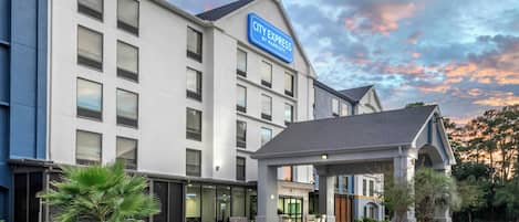 A modern hotel with a blue sign, a covered entrance, and a landscaped area with plants.