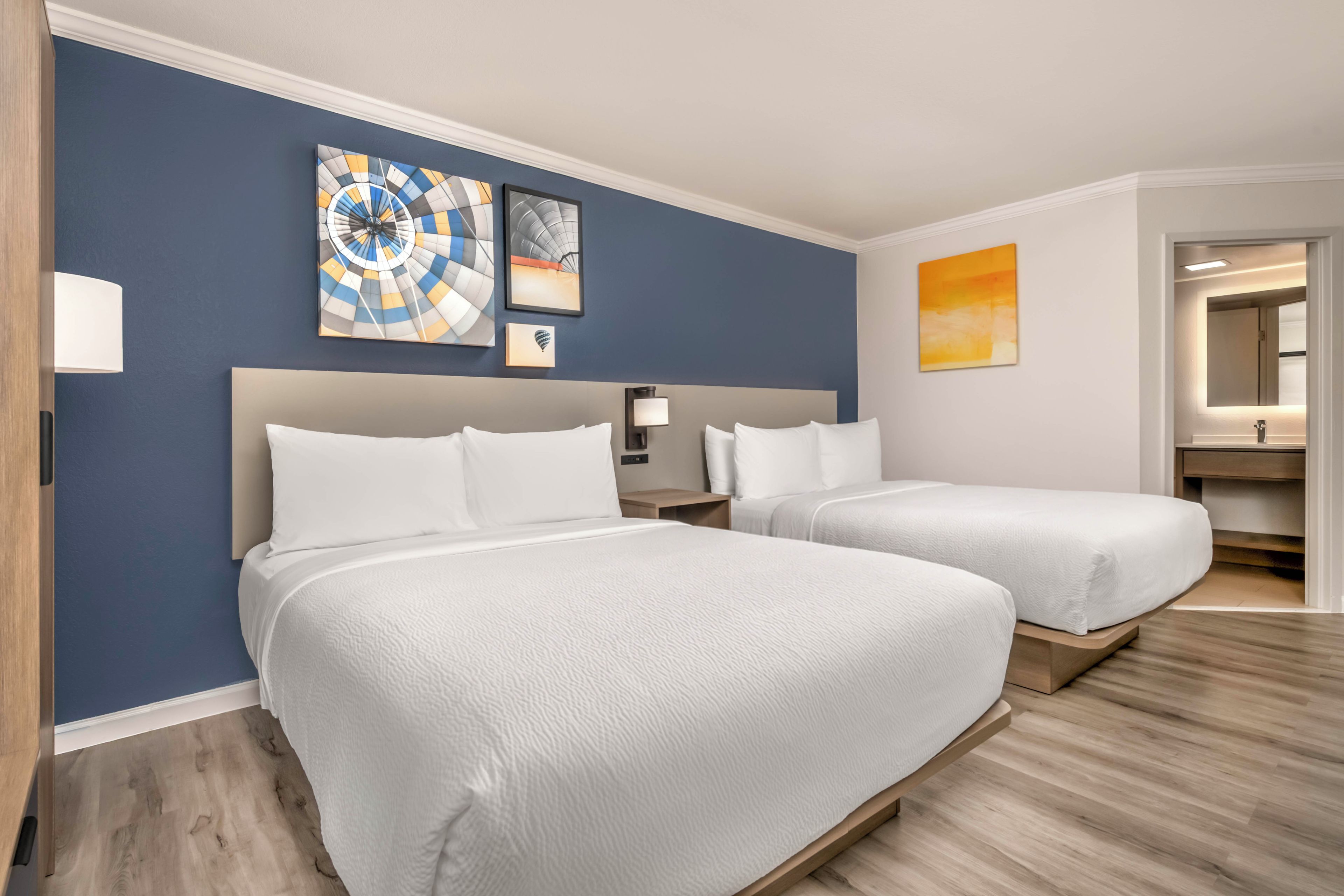 A hotel room with two beds, a nightstand, a lamp, and wall art.