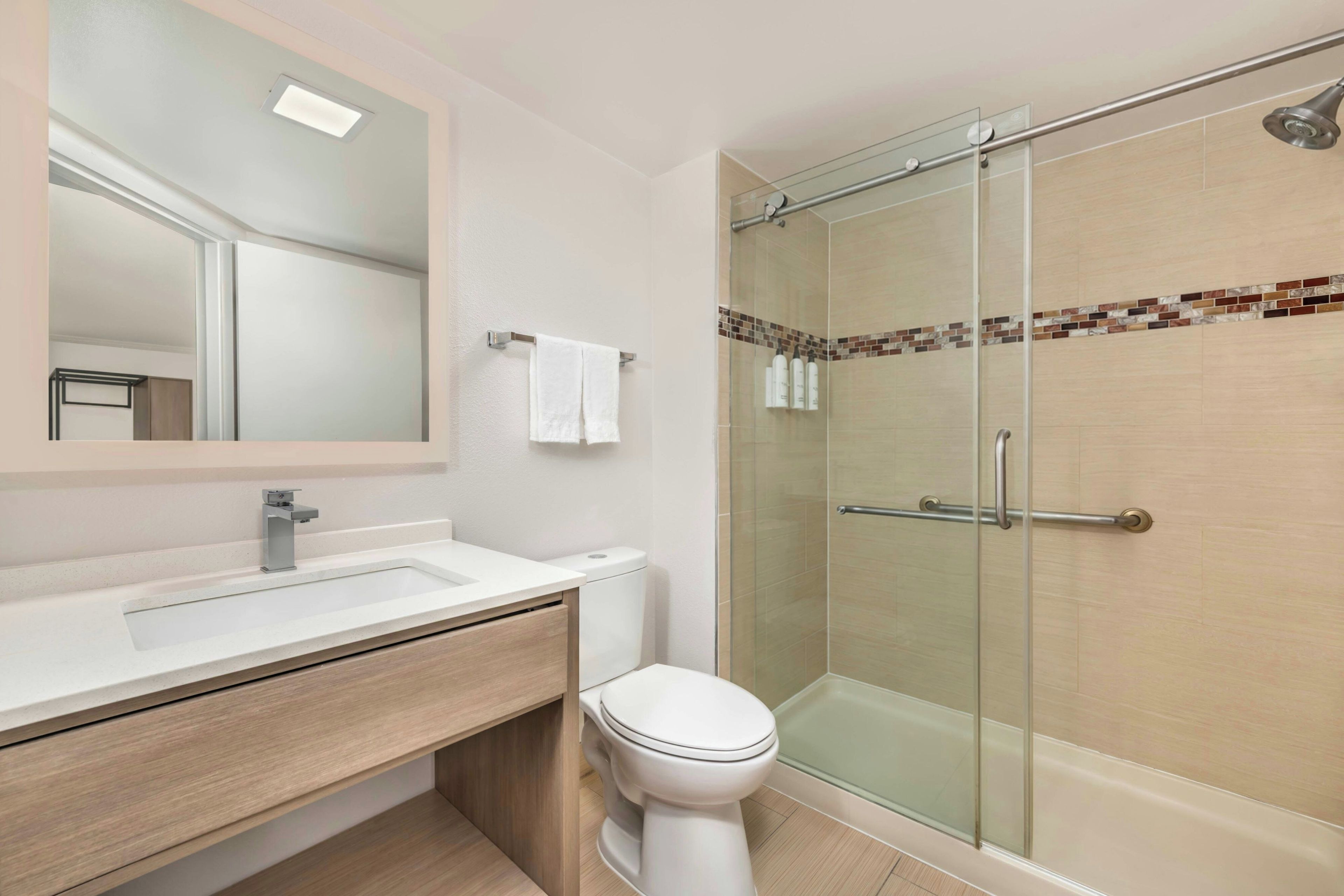 A modern bathroom with a glass-enclosed shower, a white toilet, and a vanity with a mirror.