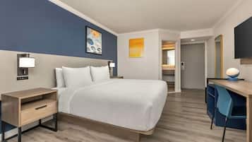A hotel room with a bed, bedside tables, a desk, a chair, and a mirror.