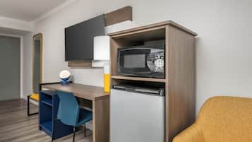 Uma cozinha compacta equipada com micro-ondas, mini-geladeira, mesa e cadeira.