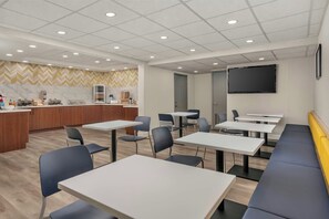 A modern dining area with tables and chairs, a kitchen area with marble countertops, and a large screen on the wall. - City Express by Marriott I-10 West Energy Corridor (Houston)
