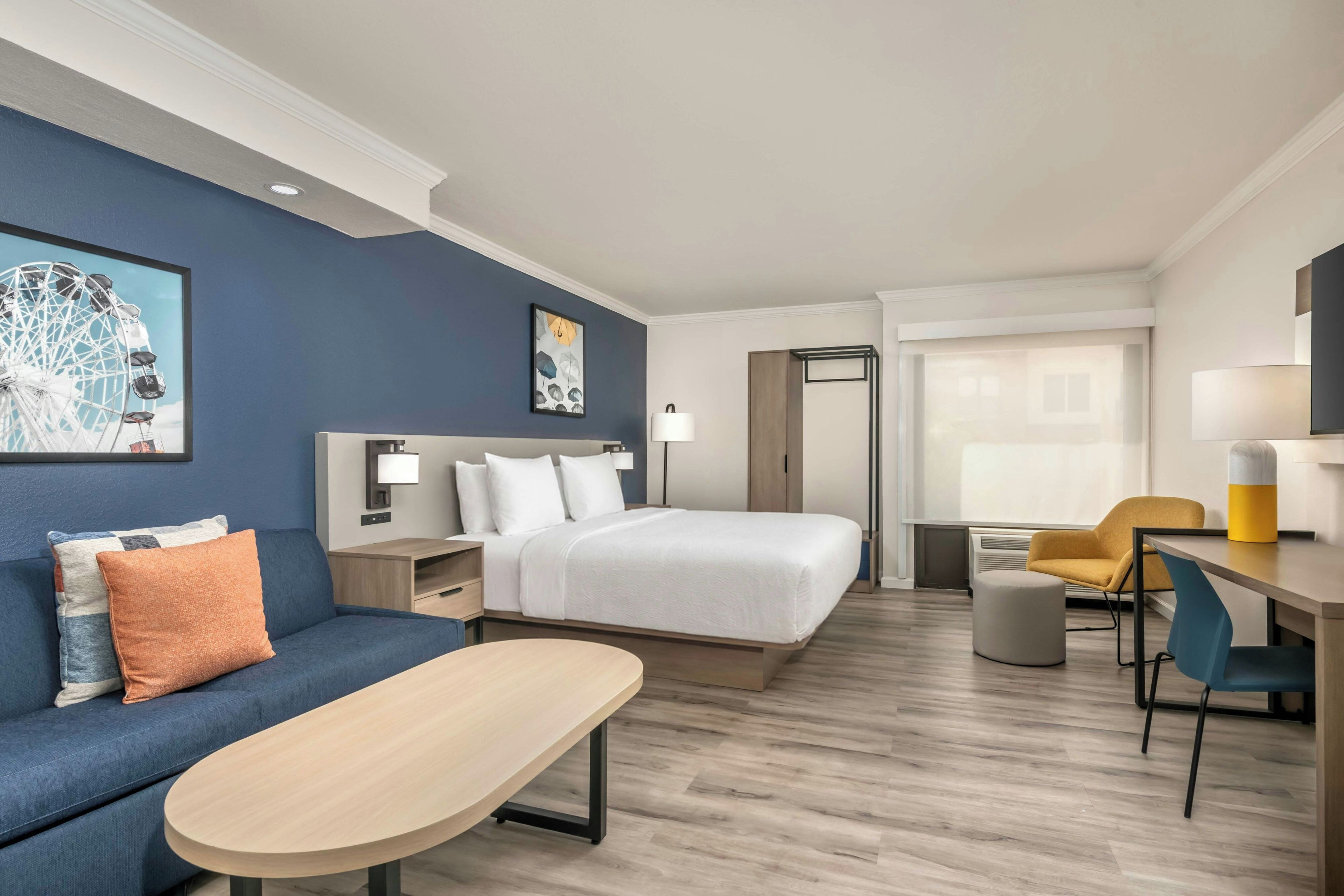 A hotel room with a bed, a desk, a chair, a sofa, and artwork on the walls.