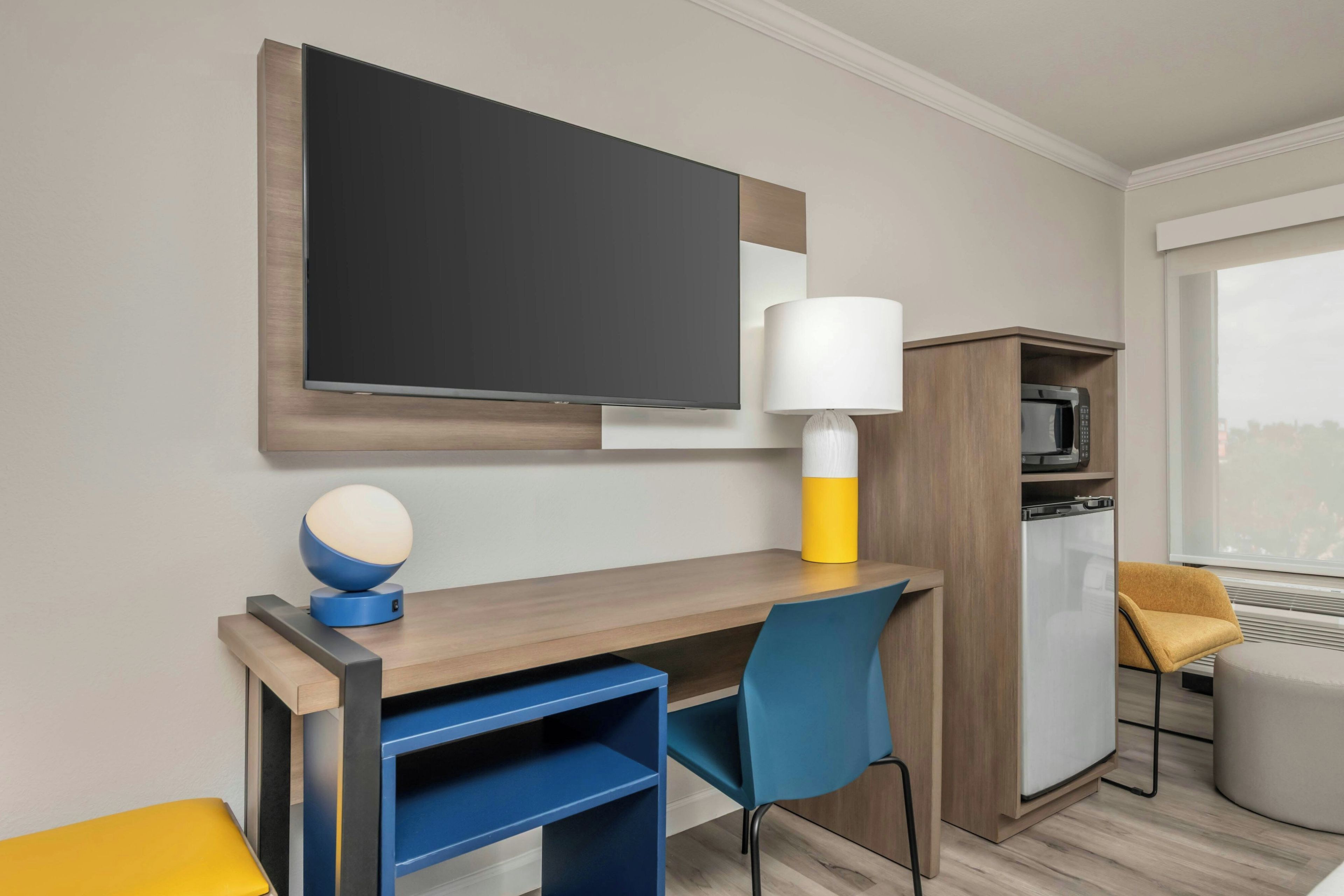 Une chambre d’hôtel équipée d’un bureau, d’une chaise, d’une télévision, d’une lampe, d’un four à micro-ondes et d’un canapé.