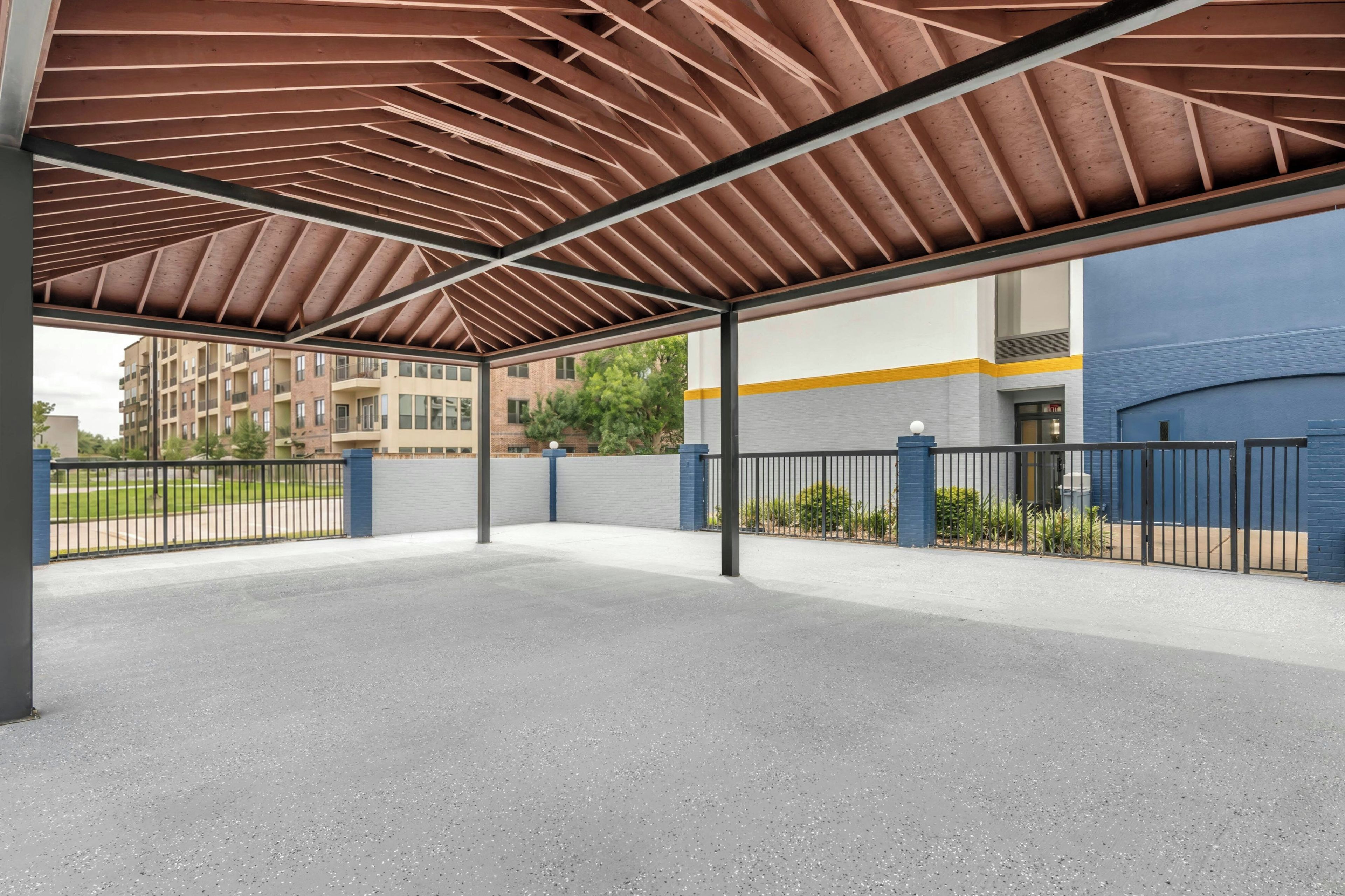 An open covered parking area with a metal roof structure, concrete floor, and surrounding walls.
