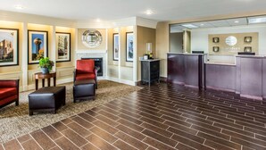 Un hall d’hôtel comprenant un comptoir d’accueil, un espace détente avec des fauteuils et des poufs, des tableaux encadrés aux murs et une cheminée.