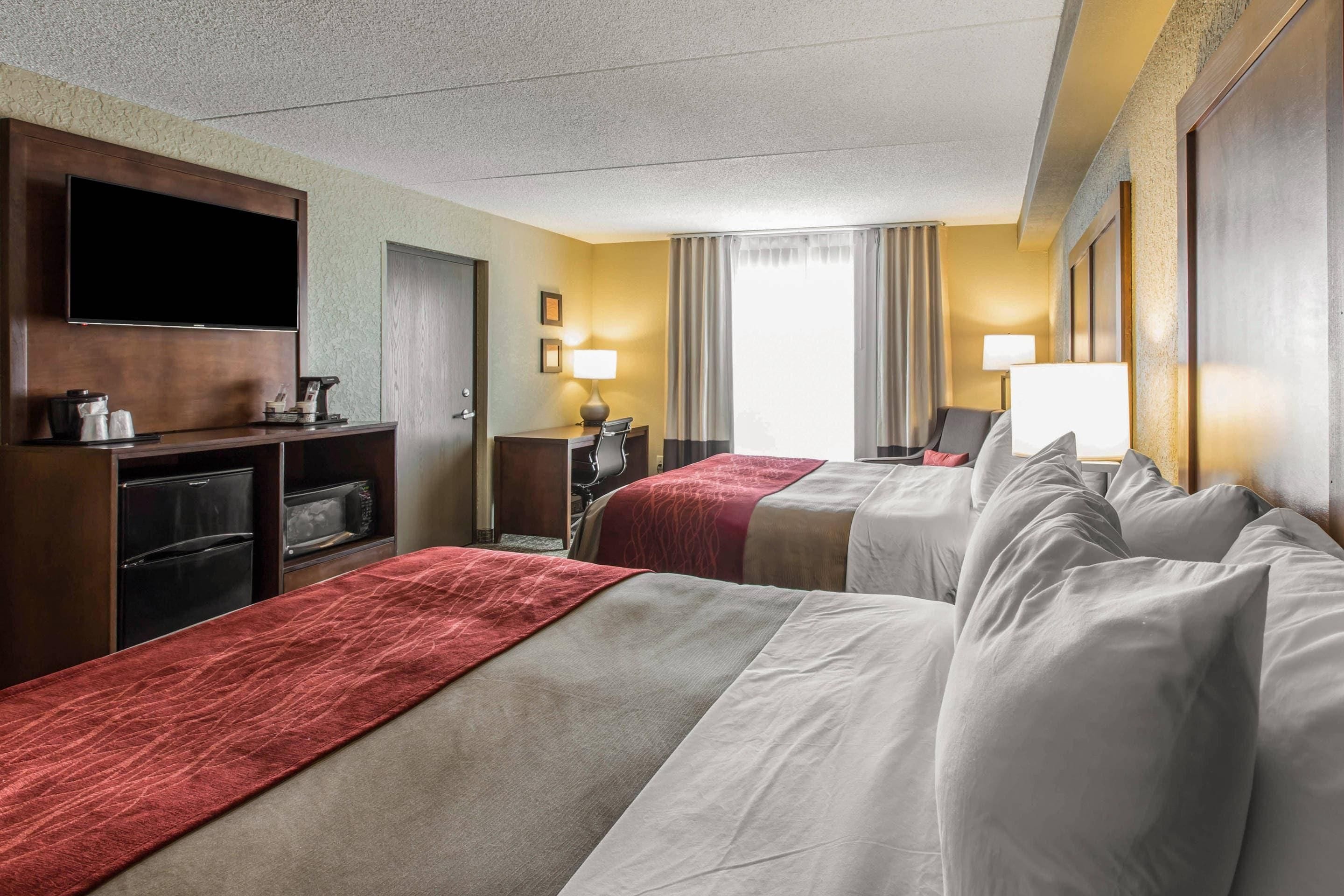 Une chambre d’hôtel avec deux lits, un téléviseur à écran plat, un bureau avec une lampe et un minibar.