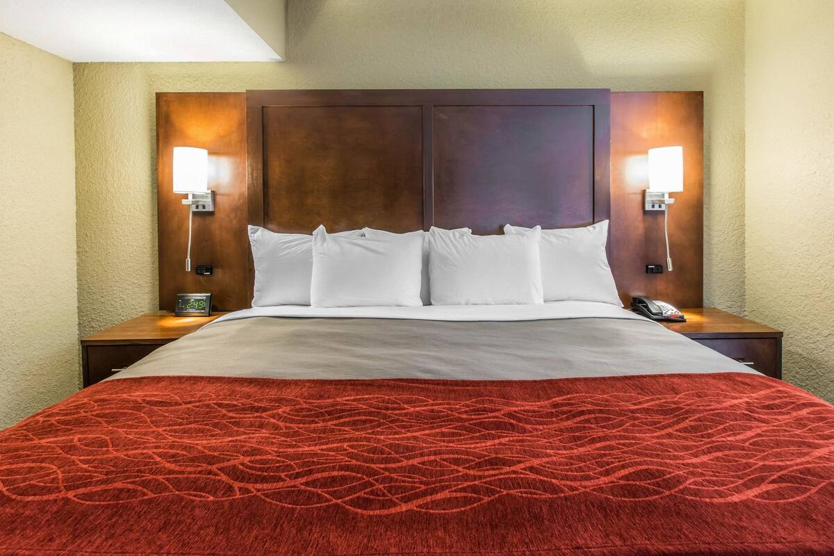 Habitación de hotel con una cama grande, dos mesitas de noche, una lámpara de noche y una colcha roja estampada, además de dos lámparas fijadas a la pared.