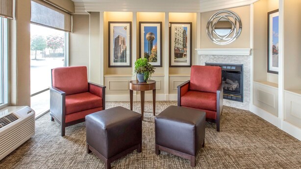 Un hall d’hôtel avec deux fauteuils rouges, une petite table sur laquelle est posée une plante, des tableaux encadrés au mur et une cheminée.