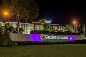 Un hotel Comfort Inn & Suites con un letrero iluminado grande, rodeado de árboles y bien iluminado por farolas.