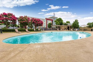Una piscina con sillones de descanso y un edificio de hotel al fondo.