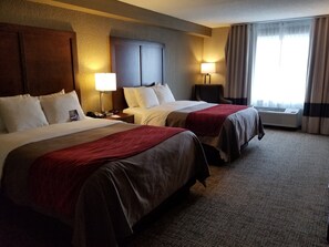 Habitación de hotel con dos camas, un escritorio, una silla, una lámpara y un equipo de aire acondicionado.