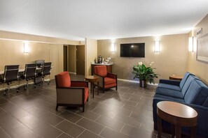 Un hall d’hôtel comprenant un espace salon, un téléviseur fixé au mur et un comptoir de réception.