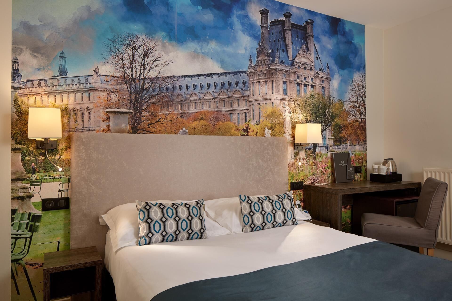 A hotel room with a large bed, two bedside lamps, a desk with a lamp, a chair, and a large painting of a building.