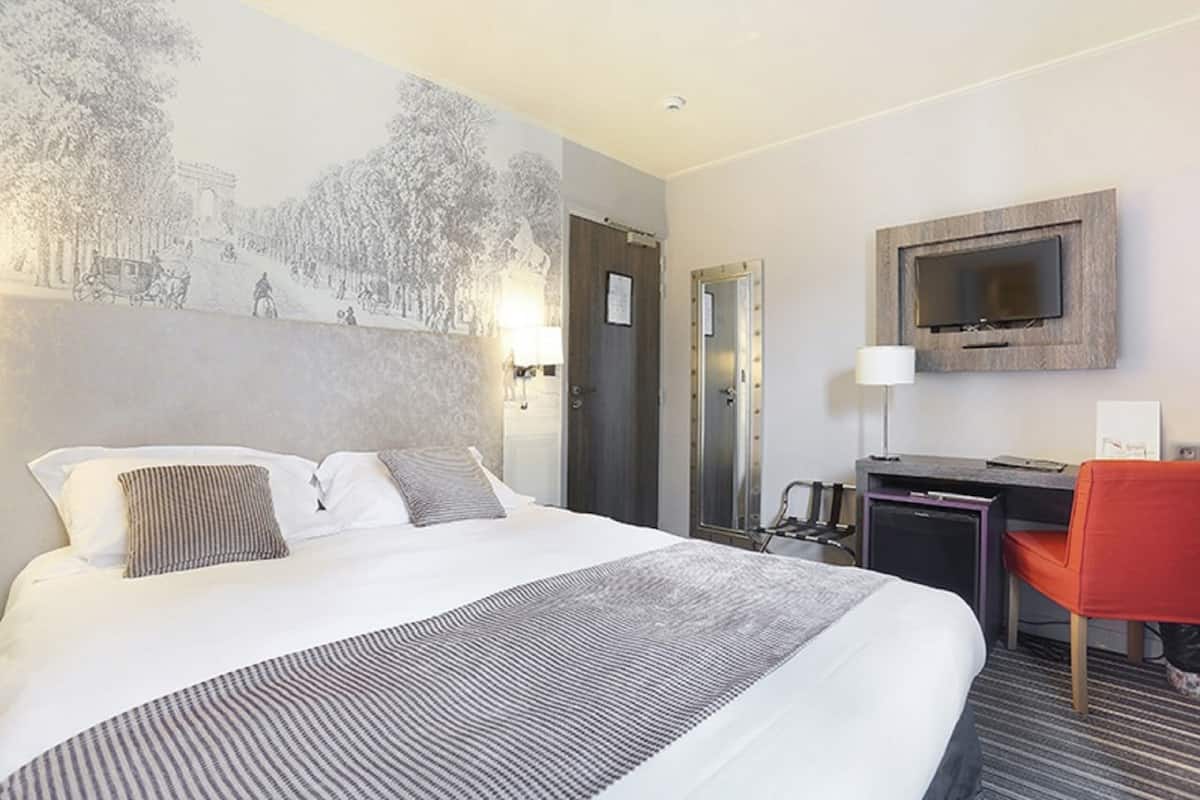 Habitación de hotel con una cama grande, un escritorio con computadora, un televisor montado en la pared y una silla roja.