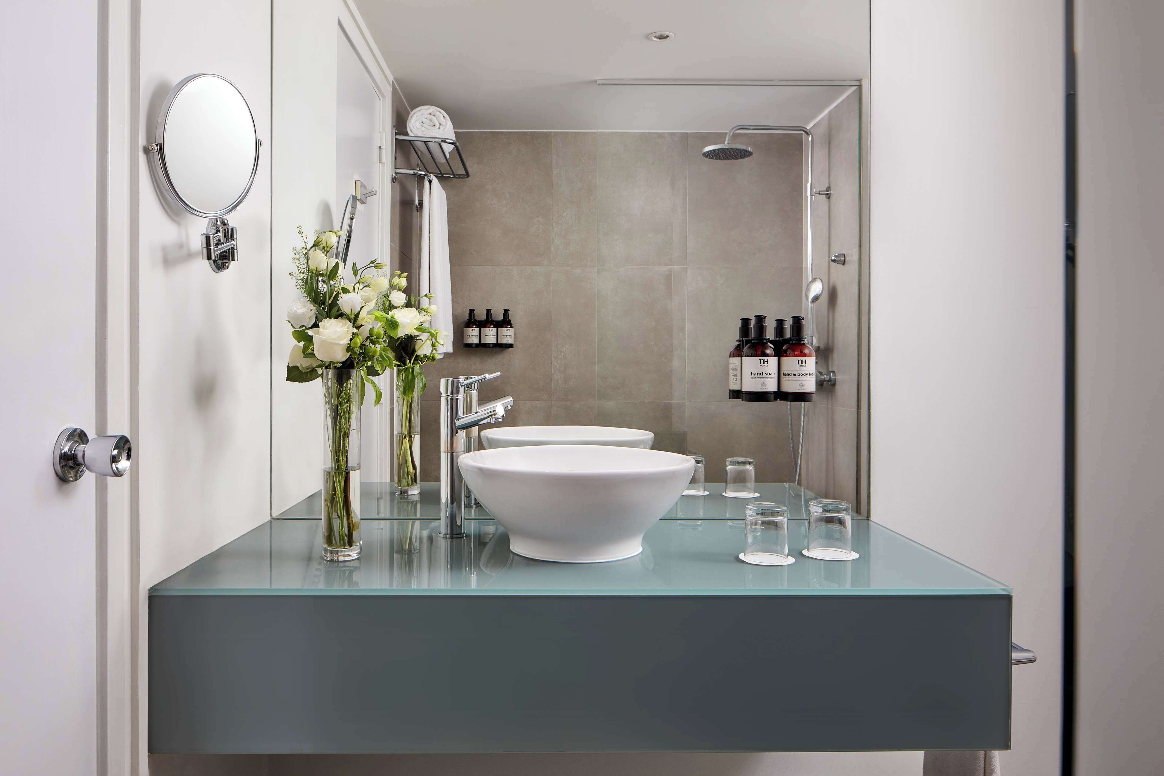 A modern bathroom with a glass countertop, two sinks, a shower, and a mirror.