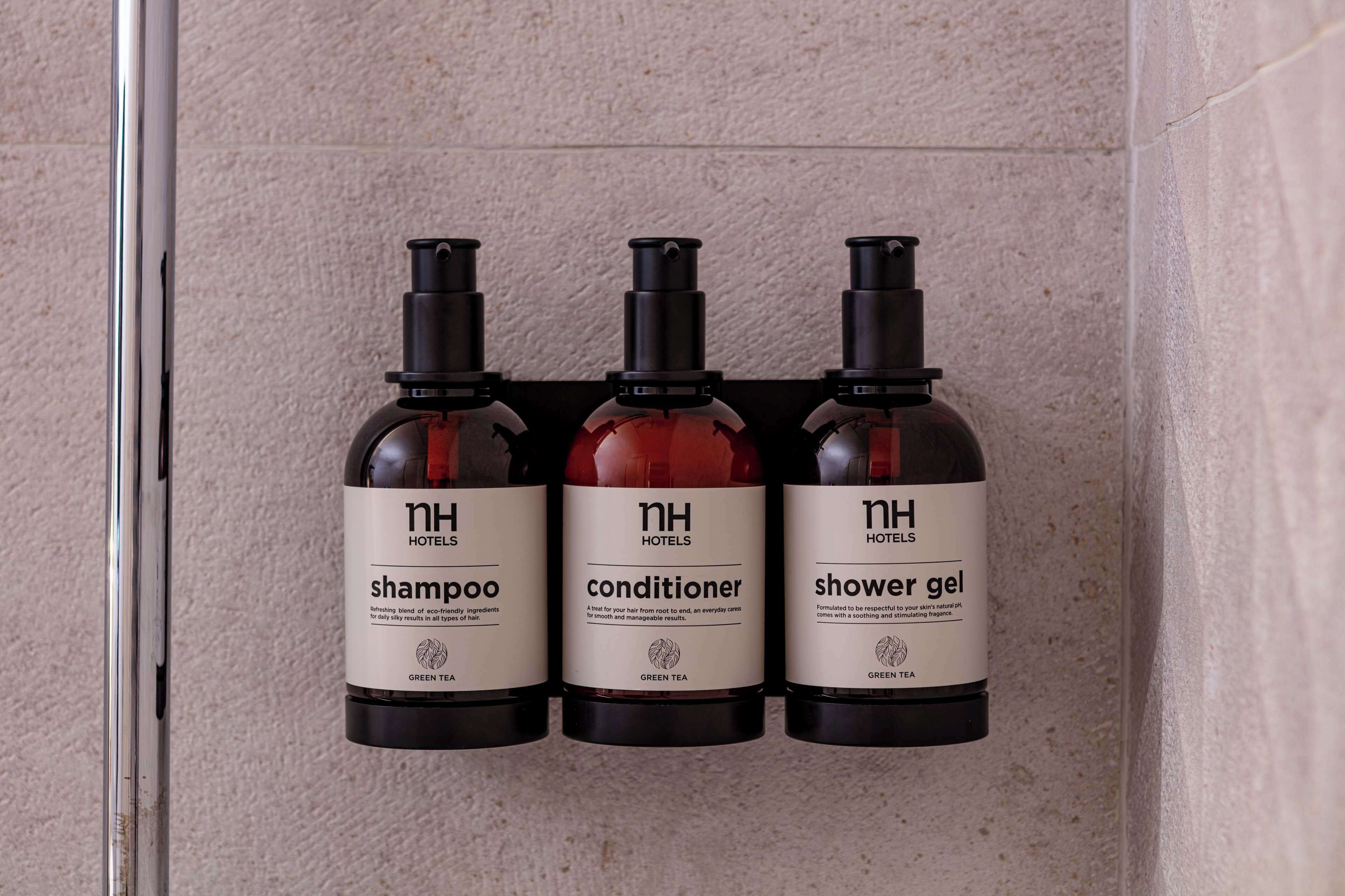 Three bottles of hotel amenities: shampoo, conditioner, and shower gel, all labeled with the hotel's name and 'green tea'.
