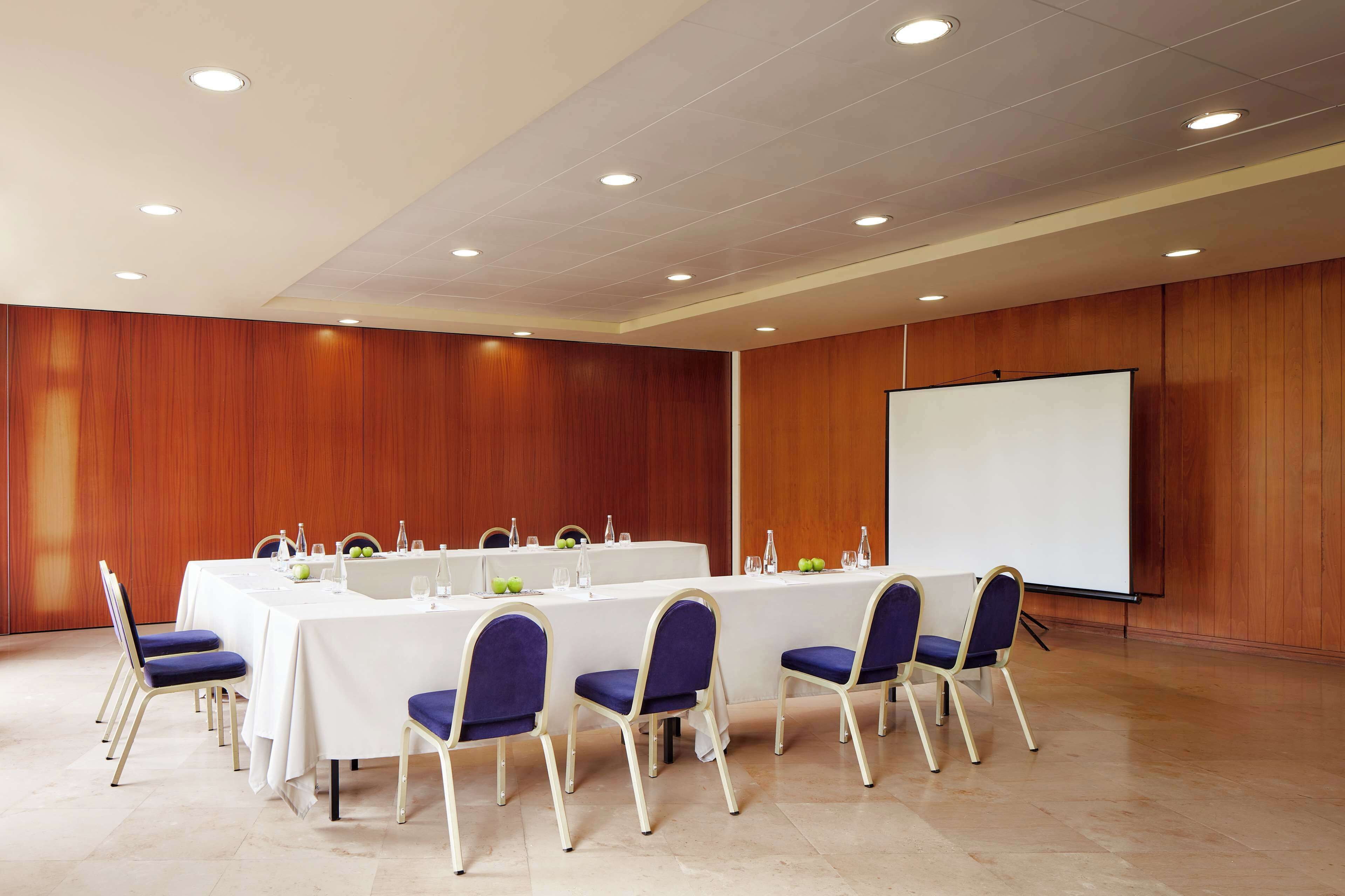 A conference room with a long table, chairs, a projector screen, and a whiteboard.