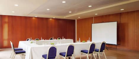 A conference room with a long table, chairs, a projector screen, and a whiteboard.
