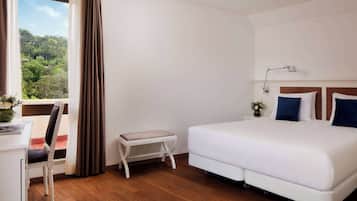 Una camera d'albergo con un letto, una scrivania, una sedia, un tavolino e una finestra con tende.