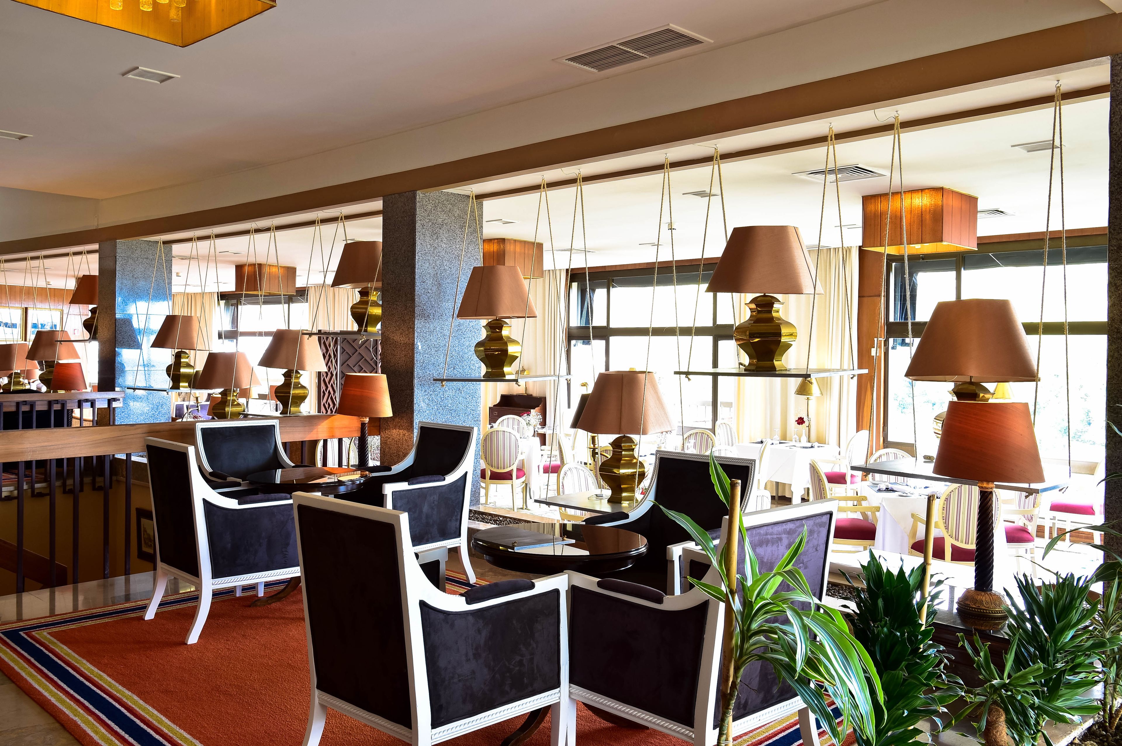 Eine Hotelhalle mit mehreren Sitzbereichen, darunter runde Tische und Stühle, sowie einer Bar.
