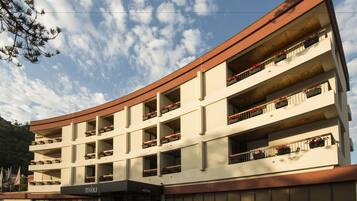 Un hotel de varios pisos con balcones, techo plano y un estacionamiento al frente.