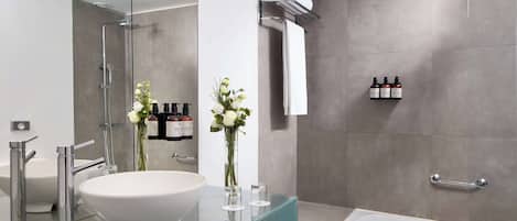 Uma casa de banho moderna com uma grande lavatório branco, toucador de vidro, chuveiro com porta de vidro e uma banheira.