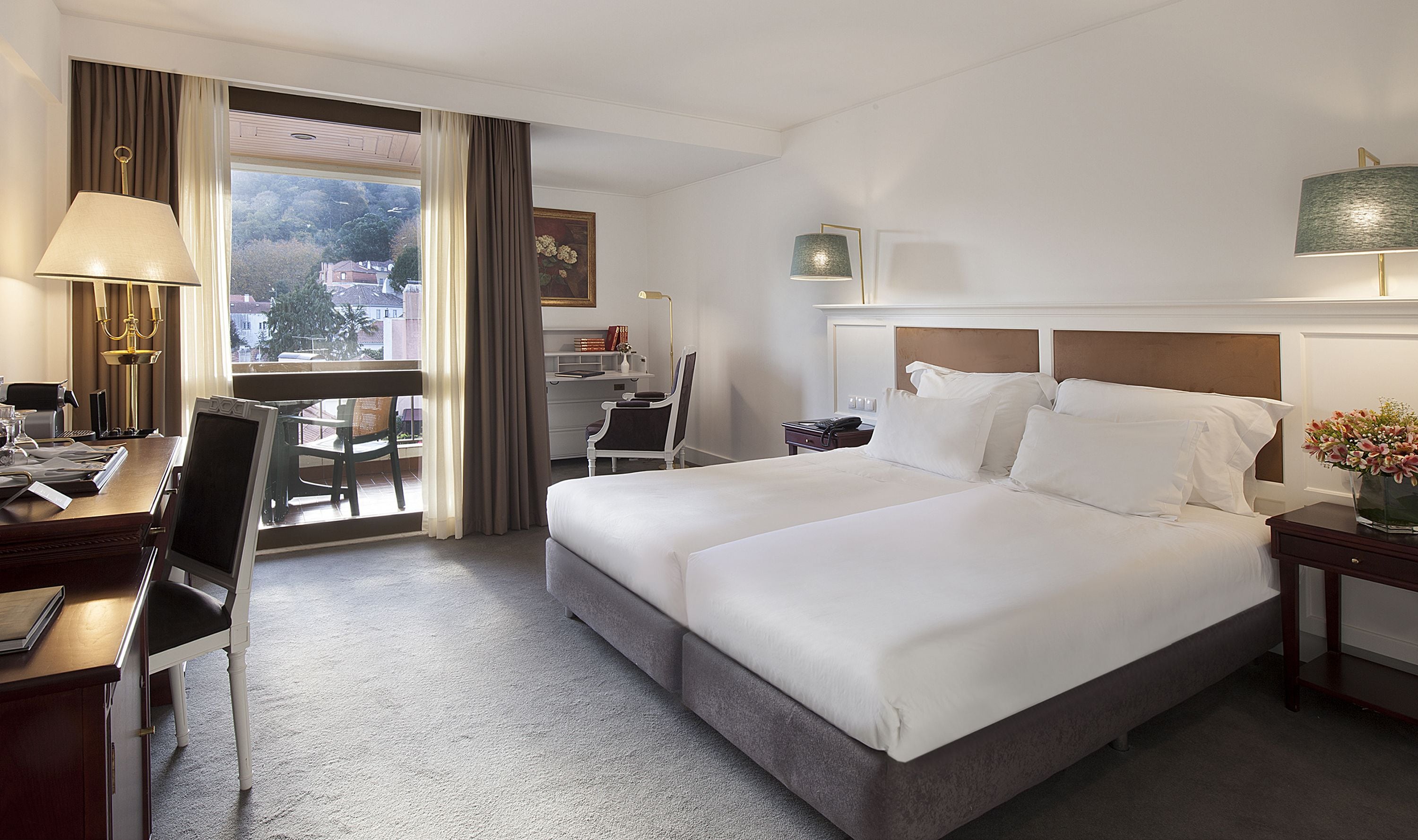 A hotel room with a large bed, a desk, a chair, a lamp, and a view of the outside.