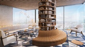 Una sala de estar moderna con una estantería de madera central, un sofá, una mesa de centro y vistas de la ciudad a través de amplios ventanales.