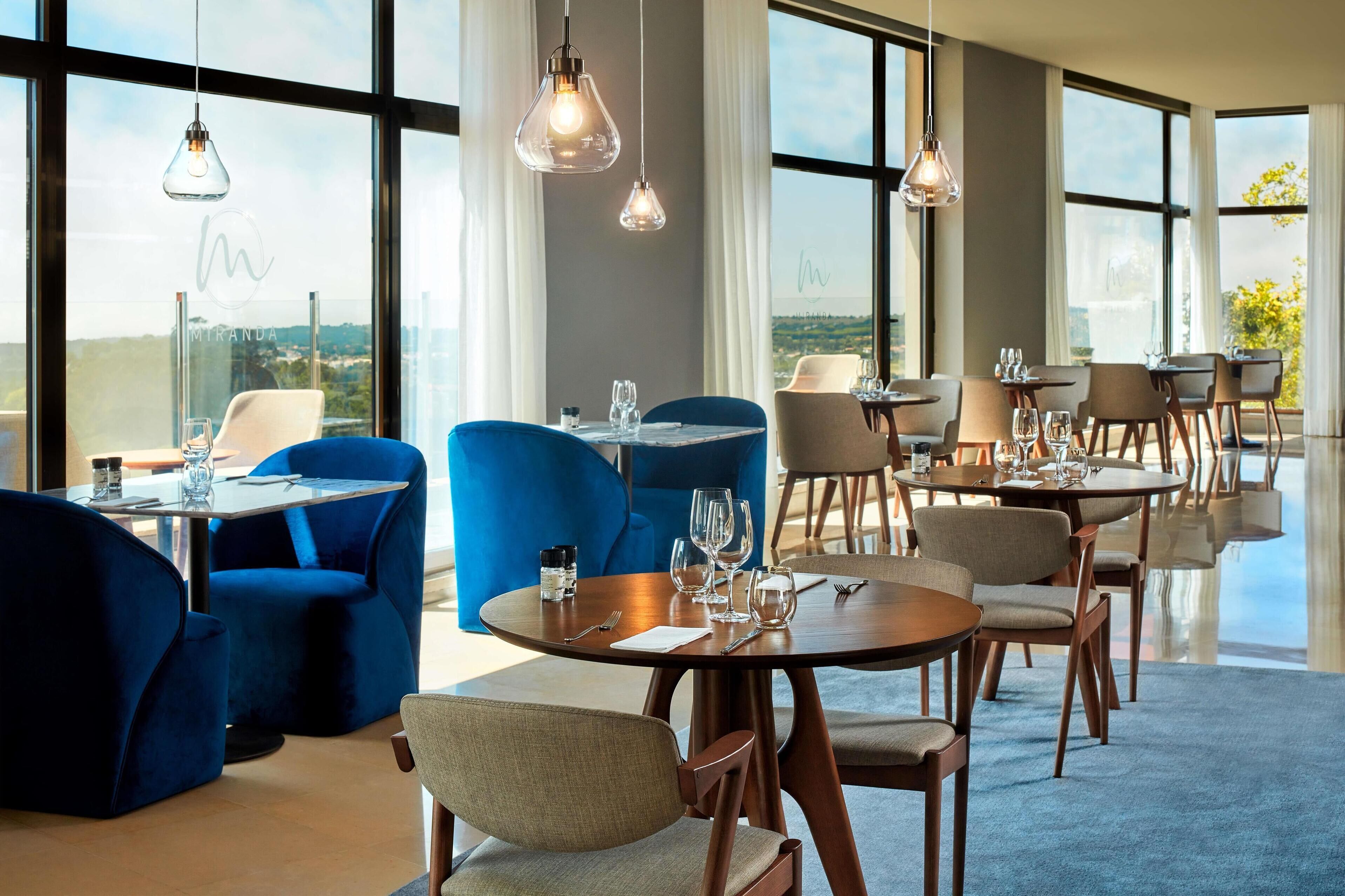 Un restaurante con mesas redondas, sillas grises y azules, y lámparas colgantes.