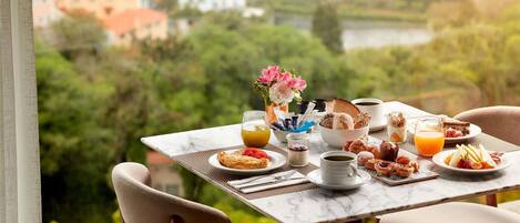 A breakfast table with various dishes, a vase of flowers, and a scenic view of buildings and greenery.