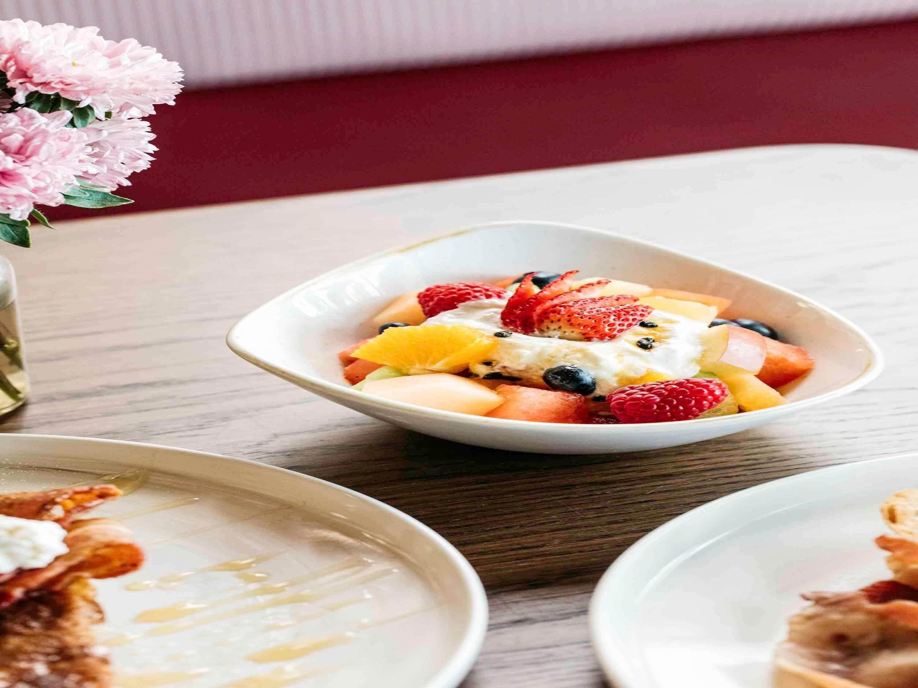 A bowl of fruit salad with yogurt on a wooden table.