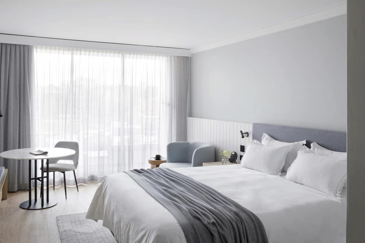 A hotel room with a bed, bedside table, chair, and a view through the window.