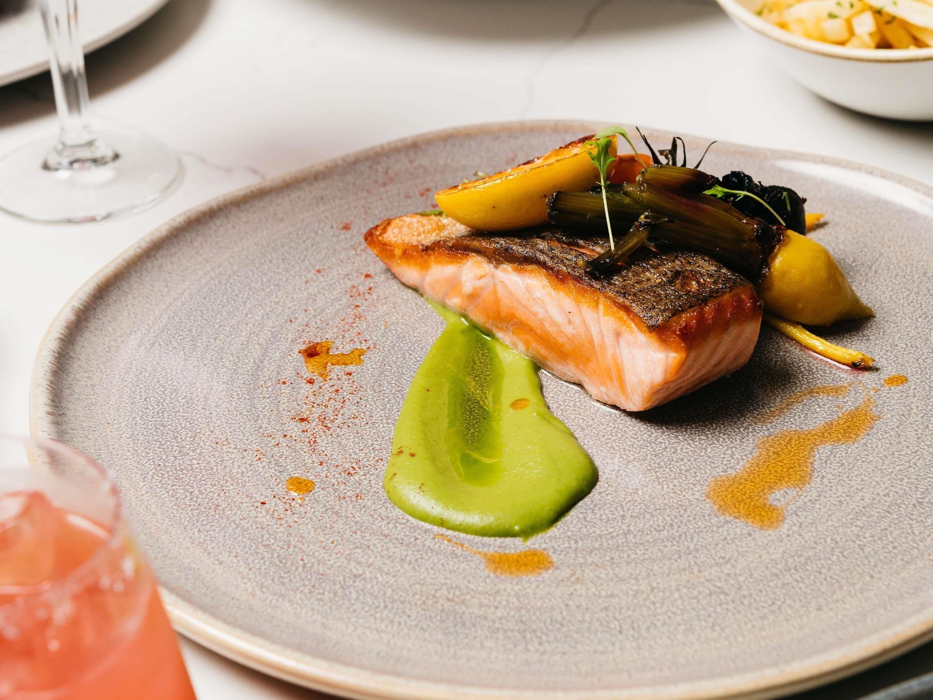 Un plato con salmón, verduras y salsa verde.