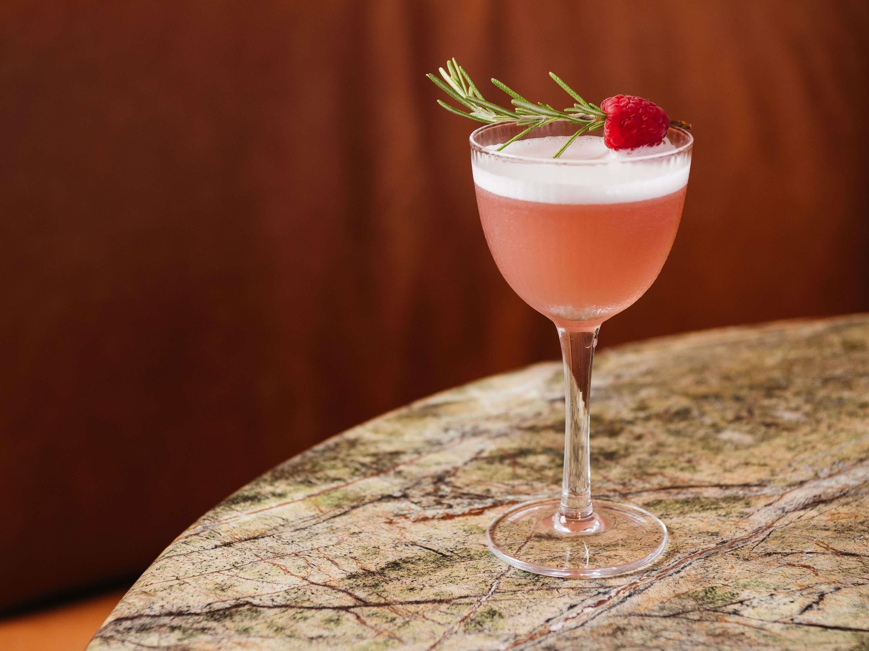 Un cocktail servi dans un verre à pied, décoré d’une fraise, posé sur une table à surface texturée.