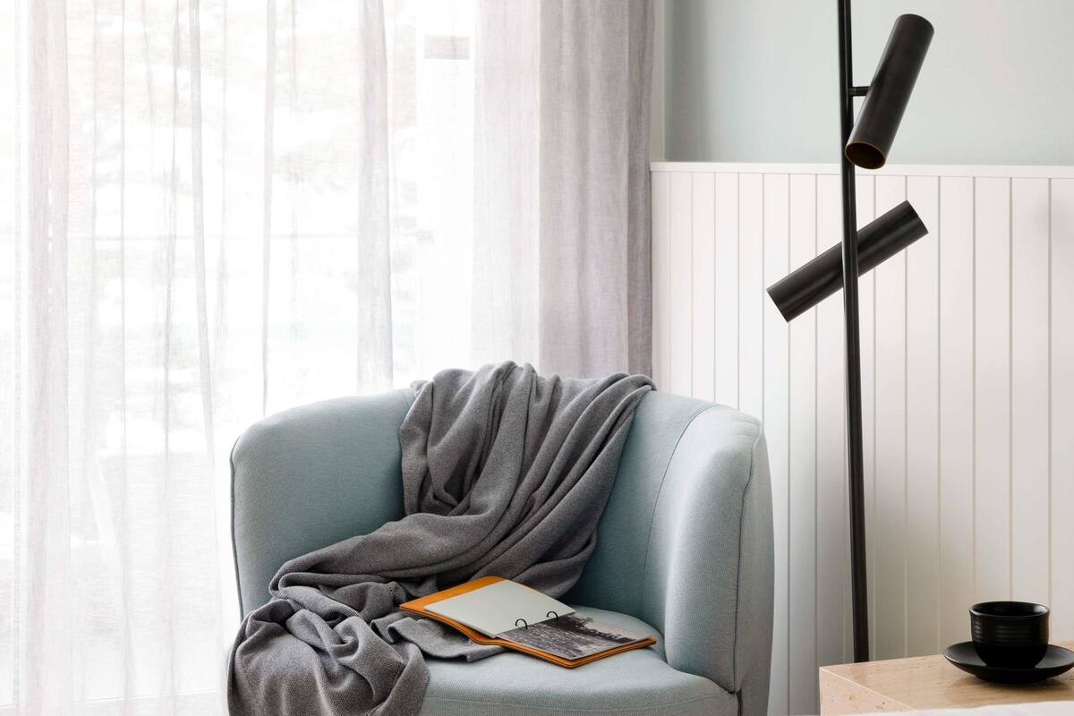 A room with a light blue armchair, a floor lamp, a notebook, and a black cup on a table.