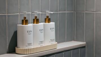 Drie witte flessen met gouden pompen op een witte plank voor een betegelde muur.