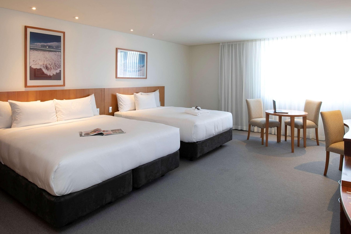 A hotel room with two beds, a small table, and a chair.