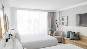 A hotel room with two beds, a chair, a bedside table, a TV, and a large window with curtains.
