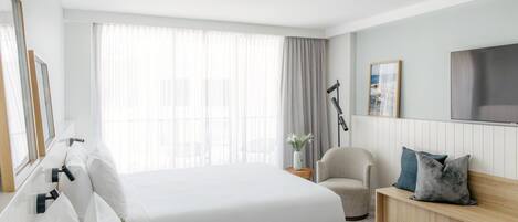 A hotel room with two beds, a chair, a bedside table, a TV, and a large window with curtains.