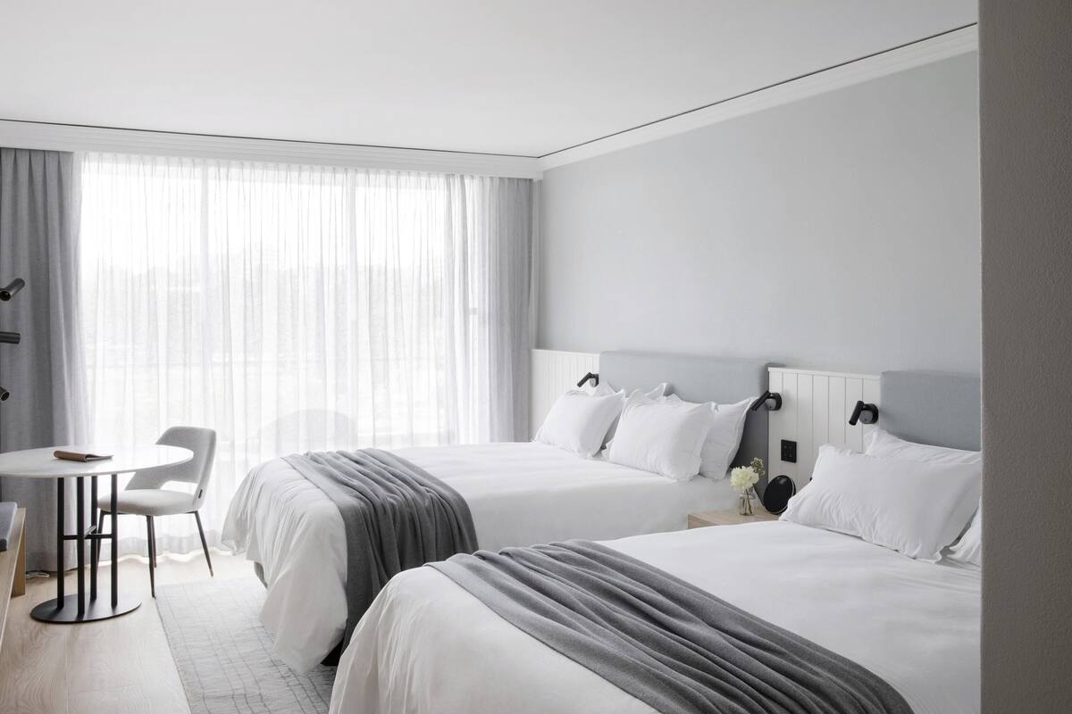 A hotel room with two beds, a small table, and a chair.