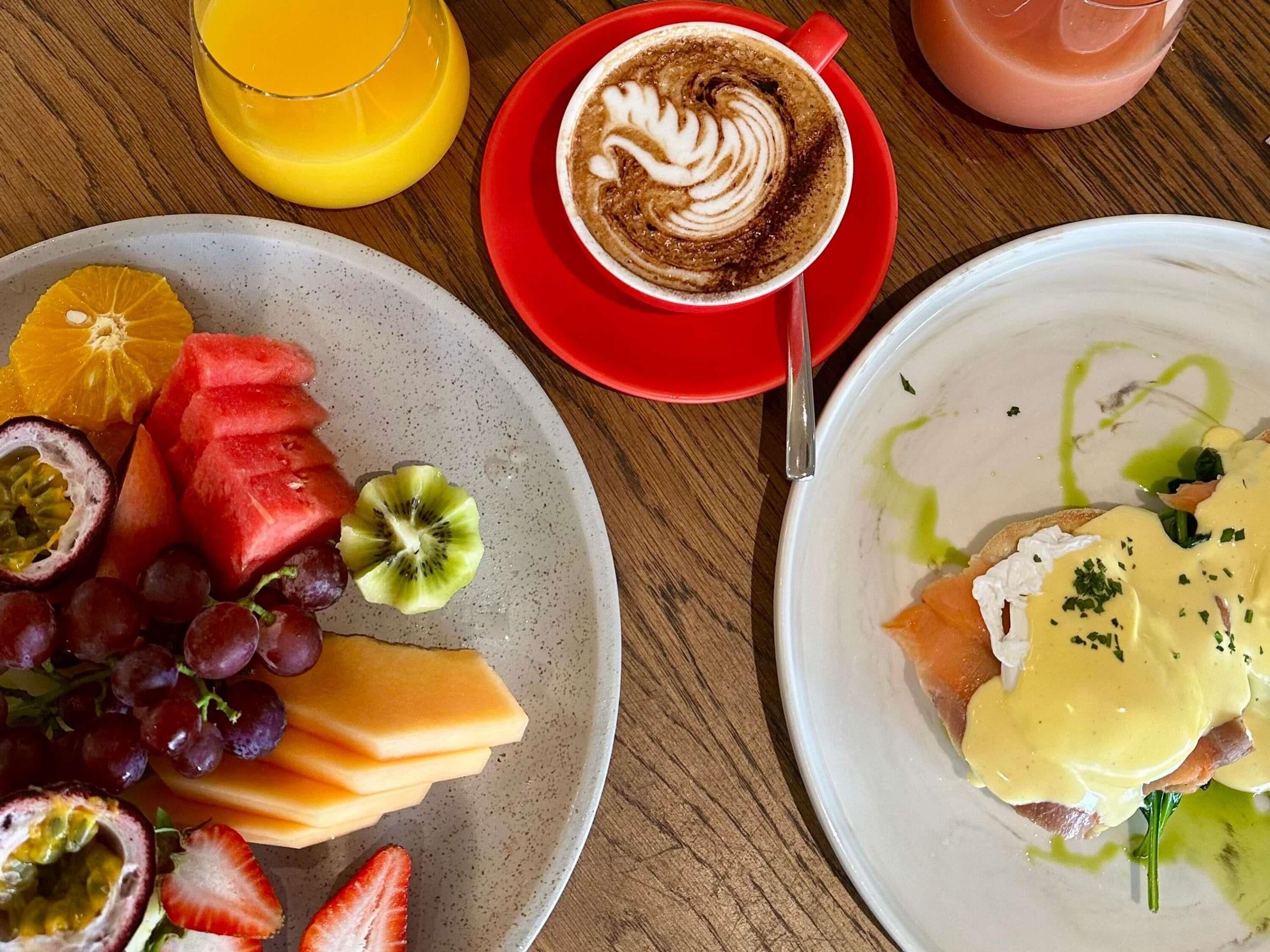 Desayuno con una fuente de fruta, una taza de café y un plato de huevos con jamón.