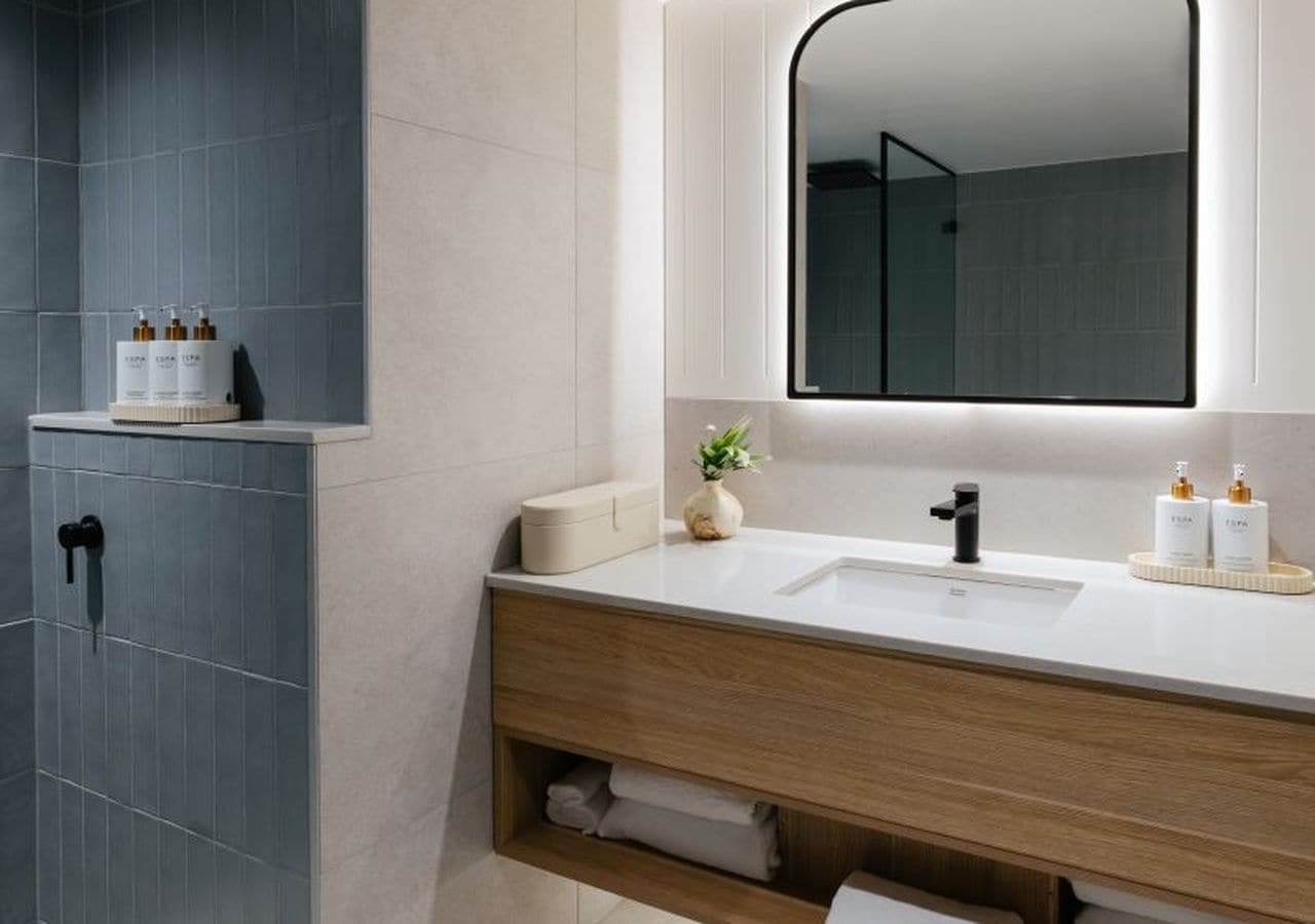 A modern bathroom with a large mirror, a sink, and a shower area.