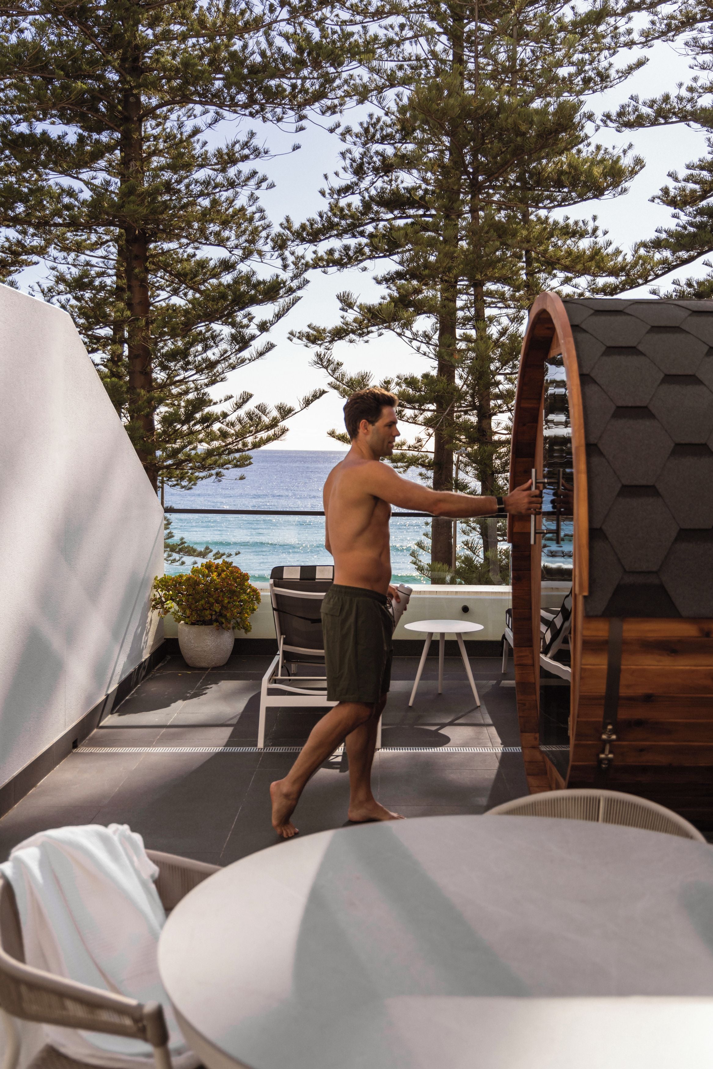 A man walking on a deck with a view of the sea, a covered seating area, and a wooden structure.