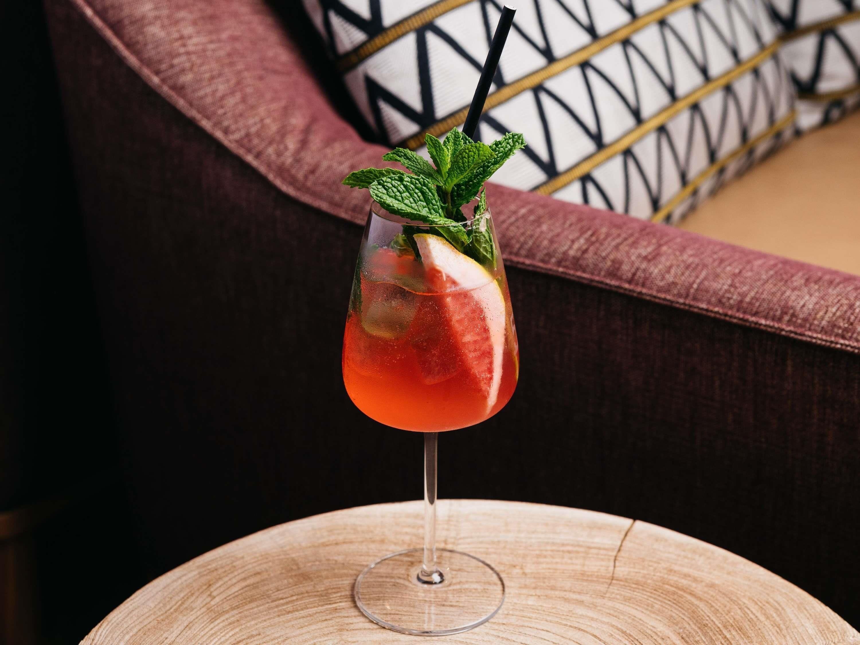 Cocktail-lasi, jossa on mintunlehti koristeena, pyöreällä puupöydällä.