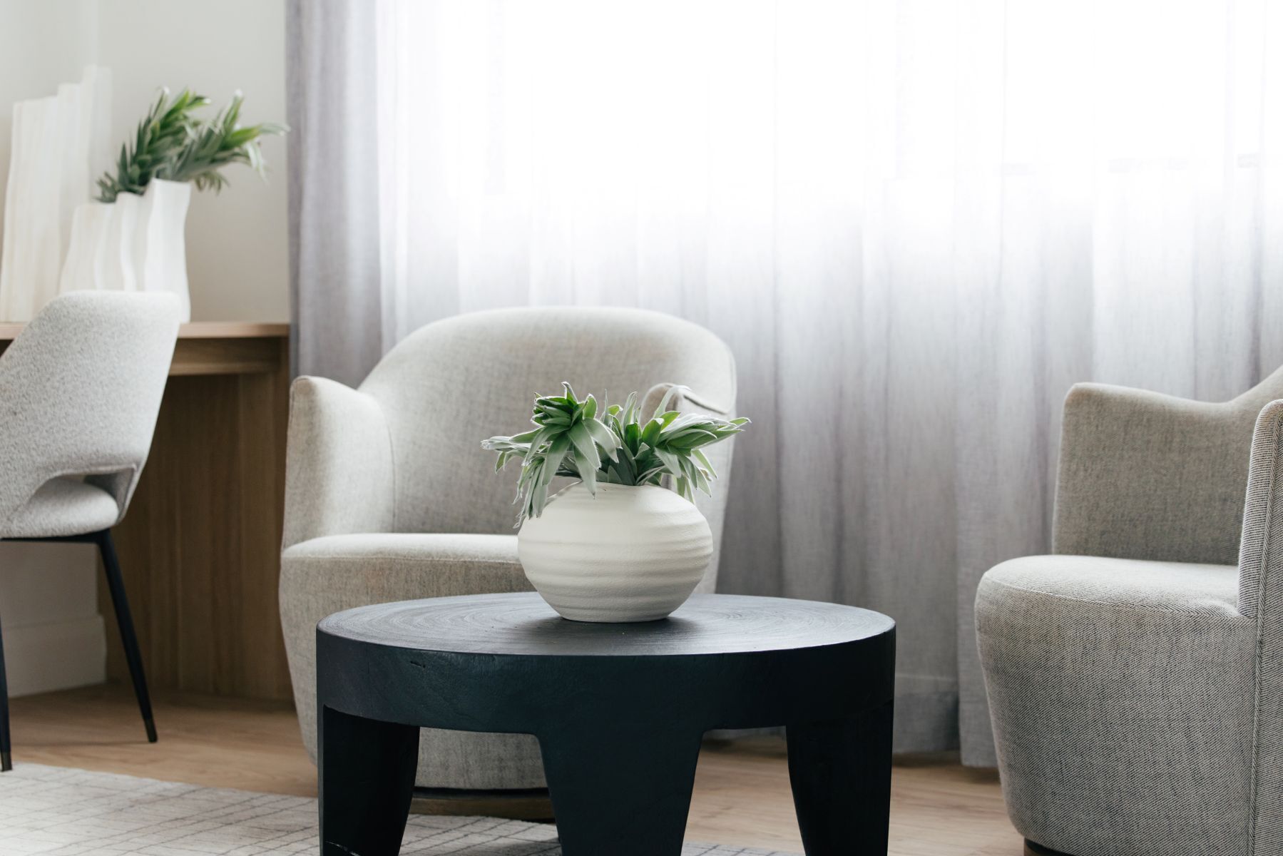Una sala de estar moderna con una mesa redonda negra, dos sillones y un jarrón blanco con plantas verdes.