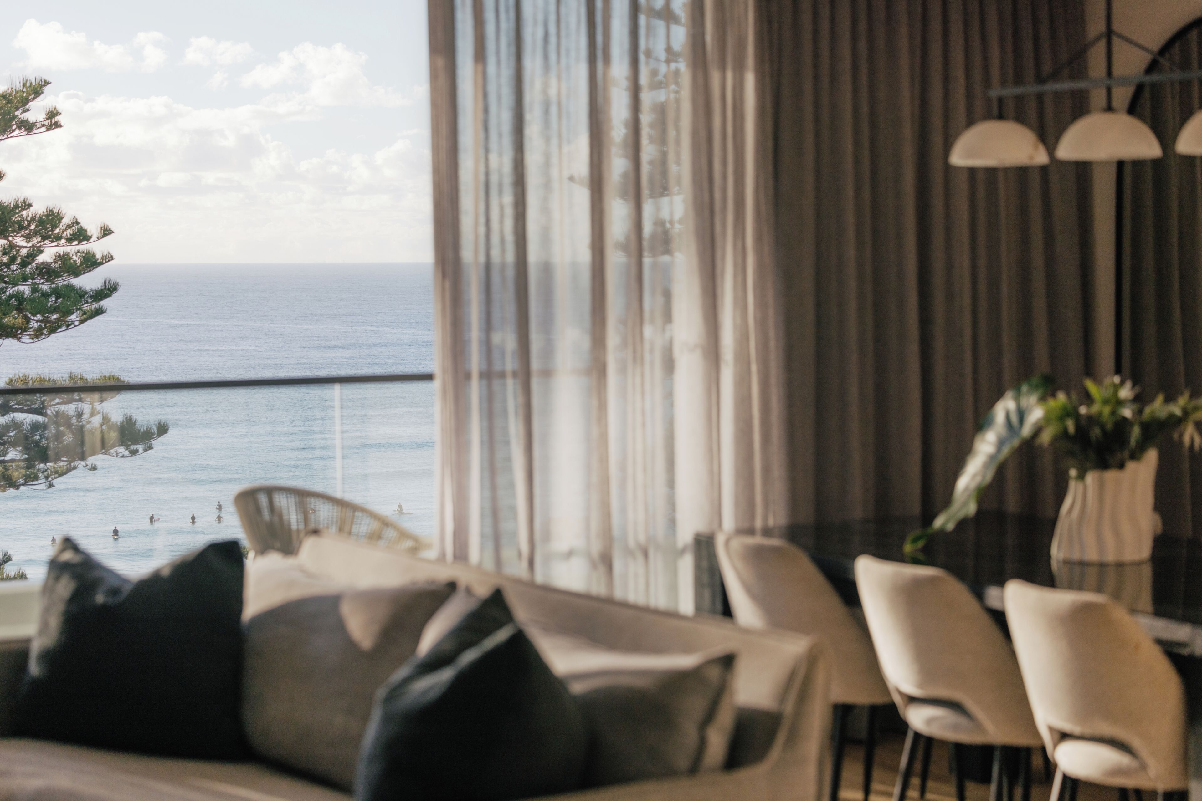 Una sala de estar moderna con vistas al mar, un comedor con sillas y un sofá con cojines.